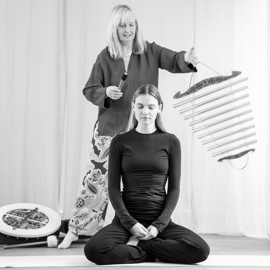 Anne Malone using a wooden chime instrument, known as a sonic chi circle, with silver bars for sound healing therapy.